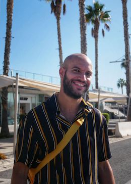 Adil portant une chemise rayée et posant devant des palmiers